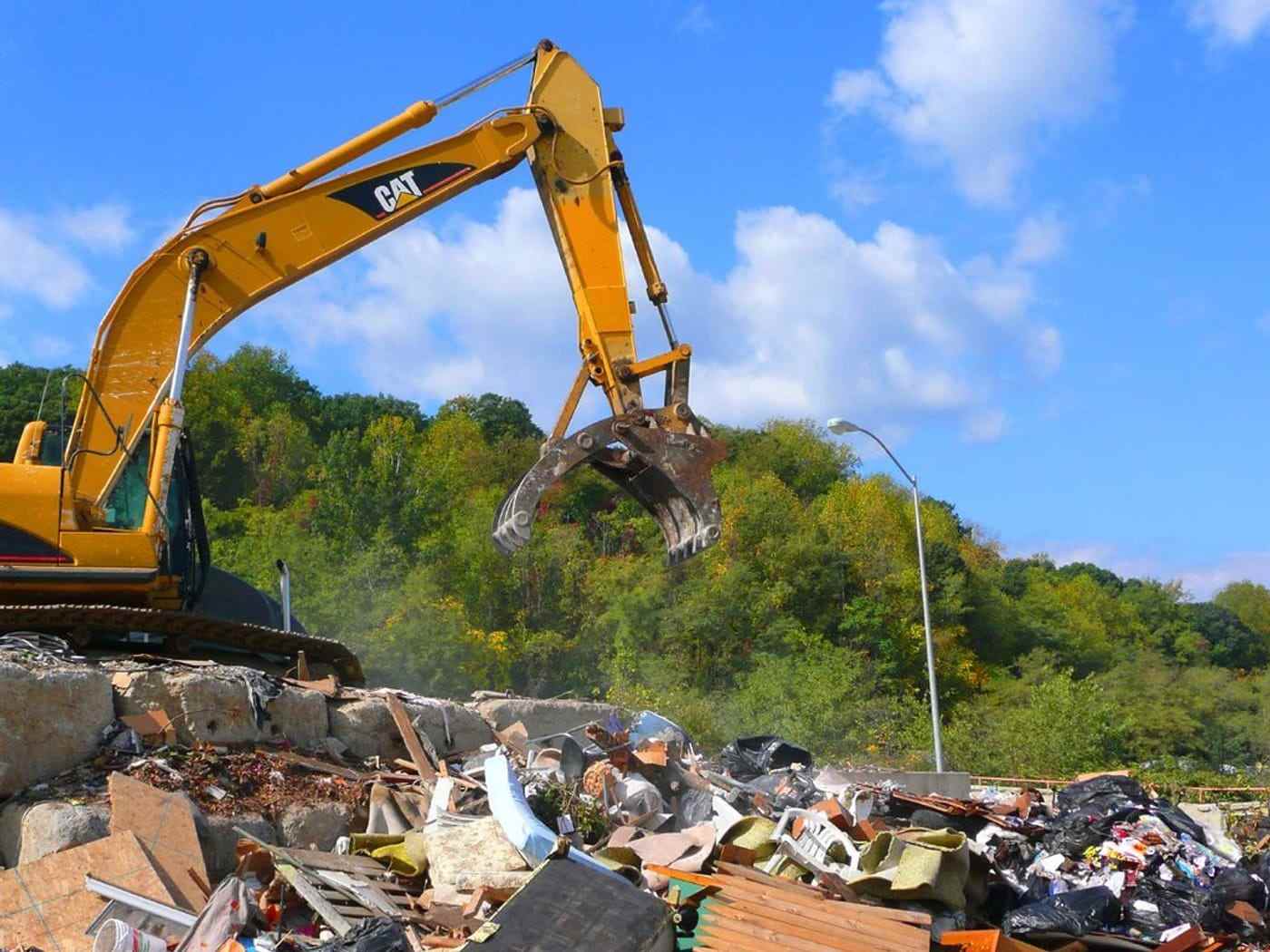 A tracked excavator with a grab sorting a pile of mixed waste